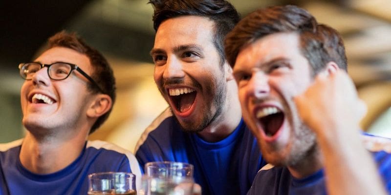 Three men laughing and drinking beer at a bar.